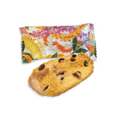 chocolate chip cookie in front of a colorful floral-patterned package on a white background