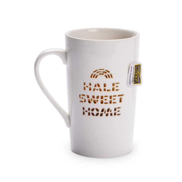 A white ceramic mug with the words 'HALE SWEET HOME' printed in brown. The mug has a slender handle and a brand tag on the side.