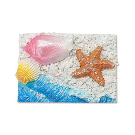A rectangular decorative magnet featuring an ocean beach scene with blue waves, white pebbles, a pink seashell, a yellow-and-white scallop shell, and an orange starfish on a white background.
